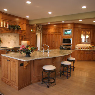 Photo of a large traditional u-shaped kitchen pantry in Cincinnati with a double-bowl sink, raised-panel cabinets, medium wood cabinets, soapstone benchtops, beige splashback, travertine splashback, stainless steel appliances, light hardwood floors, with island and beige floor.
