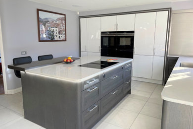 Photo of a medium sized contemporary grey and brown kitchen/diner in Hampshire with an integrated sink, quartz worktops, black appliances, ceramic flooring, an island, white floors and white worktops.