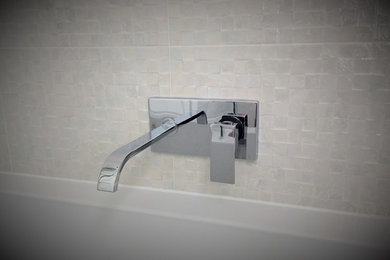 Small modern ensuite bathroom in London with a wall-mounted sink, flat-panel cabinets, white cabinets, quartz worktops, a built-in bath, a shower/bath combination, a one-piece toilet, white tiles, cement tiles, white walls and porcelain flooring.