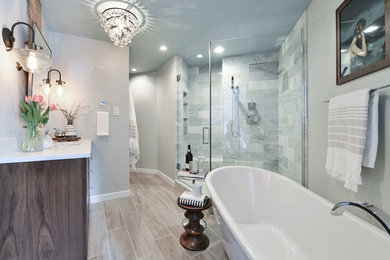 This is an example of a mid-sized transitional master bathroom in Calgary with furniture-like cabinets, medium wood cabinets, a freestanding tub, a corner shower, a one-piece toilet, white tile, porcelain tile, grey walls, porcelain floors, an undermount sink and engineered quartz benchtops.