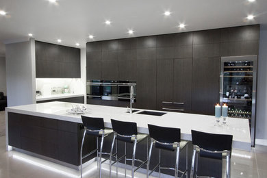 Photo of a mid-sized contemporary galley eat-in kitchen in Napier-Hastings with an undermount sink, flat-panel cabinets, dark wood cabinets, solid surface benchtops, green splashback, black appliances, ceramic floors and with island.