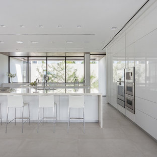 Imagen de cocina moderna, abierta, con fregadero bajoencimera, armarios con paneles lisos, puertas de armario blancas, electrodomésticos de acero inoxidable, suelo beige y dos o más islas