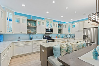 Inspiration for a large coastal u-shaped light wood floor and beige floor eat-in kitchen remodel in Miami with a farmhouse sink, flat-panel cabinets, white cabinets, quartz countertops, glass sheet backsplash, stainless steel appliances, an island and gray countertops