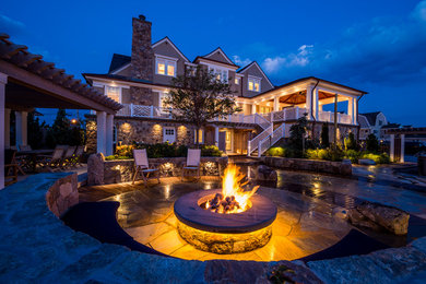 Example of a classic backyard stone patio design in New York with a fire pit and a pergola