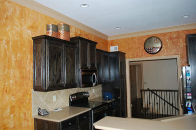 Eat-in kitchen - small mediterranean galley dark wood floor eat-in kitchen idea in Kansas City with an undermount sink, raised-panel cabinets, dark wood cabinets, solid surface countertops, brown backsplash, porcelain backsplash and black appliances