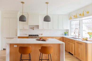 Transitional l-shaped light wood floor and beige floor kitchen photo in New York with an undermount sink, shaker cabinets, medium tone wood cabinets, white backsplash, stainless steel appliances, an island and white countertops