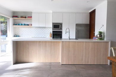 Inspiration for a mid-sized modern galley kitchen pantry in Melbourne with an undermount sink, flat-panel cabinets, white cabinets, quartz benchtops, white splashback, porcelain splashback, black appliances, slate floors, with island and grey floor.