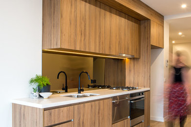 Photo of a small contemporary galley open plan kitchen in Melbourne with a single-bowl sink, beaded inset cabinets, brown cabinets, quartz benchtops, metallic splashback, mirror splashback, stainless steel appliances, vinyl floors and with island.