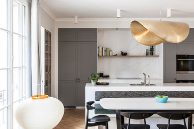 This is an example of a scandinavian galley open plan kitchen in Paris with an integrated sink, grey cabinets, quartzite benchtops, white splashback, panelled appliances, light hardwood floors, with island and white benchtop.