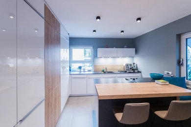 Mid-sized contemporary l-shaped separate kitchen in Frankfurt with a drop-in sink, flat-panel cabinets, white cabinets, quartzite benchtops, beige splashback, timber splashback, black appliances, ceramic floors, with island, beige floor and grey benchtop.