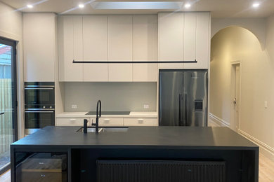 Design ideas for a mid-sized modern galley eat-in kitchen in Melbourne with a double-bowl sink, flat-panel cabinets, white cabinets, quartz benchtops, white splashback, with island, black benchtop, black appliances and light hardwood floors.