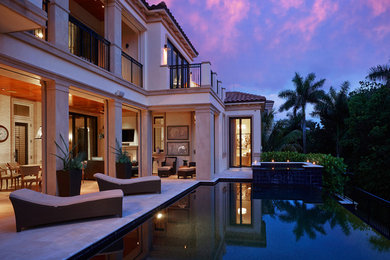 Inspiration for a large tropical backyard rectangular infinity pool in Miami with natural stone pavers and a hot tub.