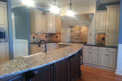 Kitchen - large modern u-shaped medium tone wood floor kitchen idea in Atlanta with a farmhouse sink, raised-panel cabinets, white cabinets, granite countertops, beige backsplash, stone tile backsplash, stainless steel appliances and an island