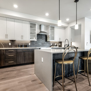 Modern l-shaped kitchen pantry in Seattle with a farmhouse sink, flat-panel cabinets, white cabinets, quartz benchtops, black splashback, ceramic splashback, stainless steel appliances, light hardwood floors, with island, brown floor and grey benchtop.
