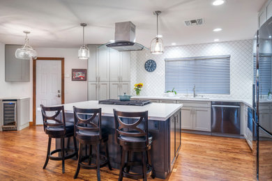 Large transitional l-shaped medium tone wood floor and brown floor open concept kitchen photo in Los Angeles with a single-bowl sink, shaker cabinets, gray cabinets, quartz countertops, white backsplash, ceramic backsplash, stainless steel appliances, an island and white countertops