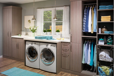 Large trendy single-wall medium tone wood floor and brown floor dedicated laundry room photo in Other with an integrated sink, flat-panel cabinets, medium tone wood cabinets, quartz countertops, gray walls and a side-by-side washer/dryer