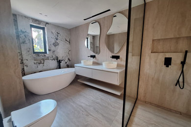 Inspiration for a large modern cream and black family bathroom in Surrey with flat-panel cabinets, beige cabinets, a freestanding bath, a walk-in shower, a wall mounted toilet, beige tiles, stone slabs, white walls, porcelain flooring, a trough sink, engineered stone worktops, beige floors, an open shower, white worktops, a feature wall, double sinks and a floating vanity unit.