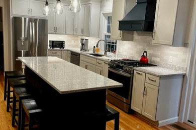 Large transitional u-shaped medium tone wood floor and brown floor enclosed kitchen photo in Boston with an undermount sink, shaker cabinets, white cabinets, quartz countertops, white backsplash, ceramic backsplash, stainless steel appliances, an island and gray countertops