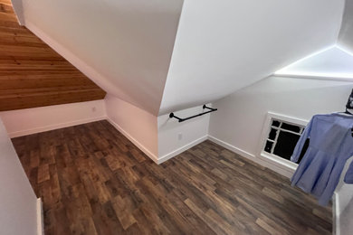 他の地域にある高級な広いコンテンポラリースタイルのおしゃれなウォークインクローゼット (オープンシェルフ、白いキャビネット、ラミネートの床、茶色い床、三角天井) の写真