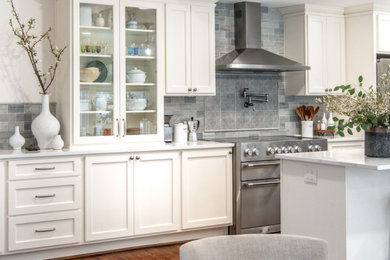 Eat-in kitchen - mid-sized traditional single-wall medium tone wood floor and multicolored floor eat-in kitchen idea in Houston with a drop-in sink, shaker cabinets, white cabinets, quartz countertops, gray backsplash, stone tile backsplash, stainless steel appliances, an island and white countertops