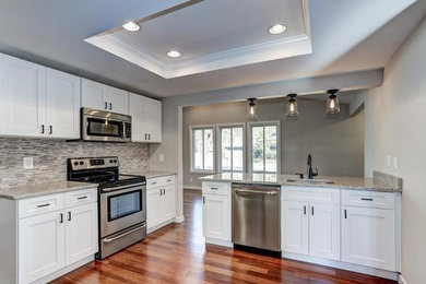 Large elegant medium tone wood floor and brown floor enclosed kitchen photo in DC Metro with an undermount sink, shaker cabinets, white cabinets, granite countertops, gray backsplash, matchstick tile backsplash, stainless steel appliances and a peninsula