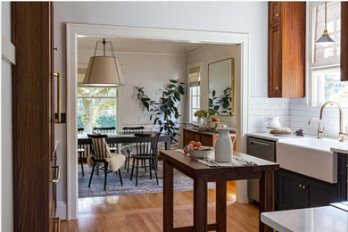 Eat-in kitchen - mid-sized traditional u-shaped light wood floor and brown floor eat-in kitchen idea in Portland with a farmhouse sink, shaker cabinets, medium tone wood cabinets, quartz countertops, white backsplash, subway tile backsplash, white appliances, an island and white countertops