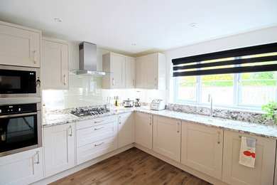 Inspiration for a medium sized contemporary u-shaped enclosed kitchen in Essex with an integrated sink, shaker cabinets, white cabinets, marble worktops, white splashback, glass sheet splashback, stainless steel appliances, laminate floors and no island.