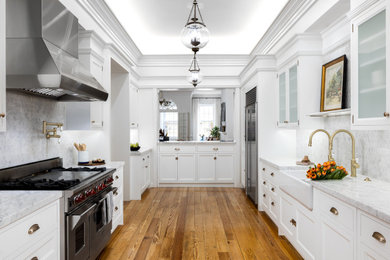 Transitional kitchen photo in Philadelphia with a farmhouse sink, white cabinets, marble countertops, stone tile backsplash, stainless steel appliances and white countertops
