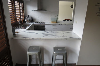 Photo of a mid-sized modern u-shaped open plan kitchen in Melbourne with a drop-in sink, flat-panel cabinets, white cabinets, laminate benchtops, white splashback, subway tile splashback, stainless steel appliances and no island.