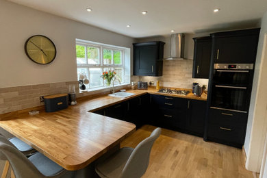 Design ideas for a medium sized modern u-shaped kitchen/diner in Oxfordshire with a submerged sink, flat-panel cabinets, blue cabinets, wood worktops, beige splashback, ceramic splashback, integrated appliances, laminate floors, a breakfast bar, brown floors and brown worktops.