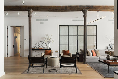 Large industrial open concept living room in New York with white walls, light hardwood floors, a two-sided fireplace, a plaster fireplace surround and a wall-mounted tv.