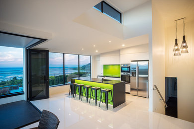 This is an example of an expansive contemporary single-wall open plan kitchen in Other with a drop-in sink, recessed-panel cabinets, white cabinets, solid surface benchtops, green splashback, glass sheet splashback, stainless steel appliances, ceramic floors and with island.