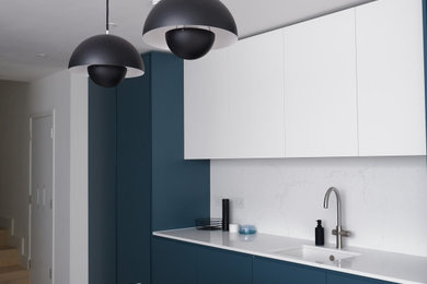 Photo of a medium sized modern single-wall open plan kitchen in London with an integrated sink, flat-panel cabinets, blue cabinets, quartz worktops, white splashback, stone slab splashback, stainless steel appliances, light hardwood flooring, an island, brown floors, white worktops, a drop ceiling and feature lighting.