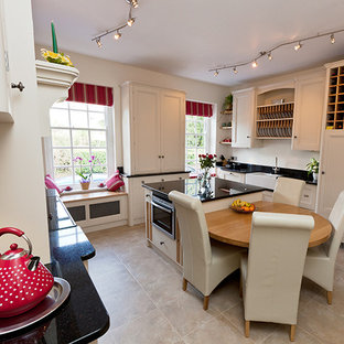 Large traditional kitchen pantry ideas - Example of a large classic u-shaped kitchen pantry design in Kent with a farmhouse sink, beaded inset cabinets, white cabinets, granite countertops, black backsplash, stone slab backsplash, stainless steel appliances and an island