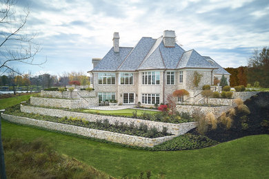 Inspiration for a french country beige three-story stone house exterior remodel in Grand Rapids with a hip roof, a shingle roof and a gray roof