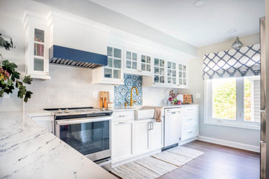 Photo of a mid-sized beach style l-shaped eat-in kitchen in Bridgeport with a farmhouse sink, quartz benchtops, blue splashback, ceramic splashback, stainless steel appliances, a peninsula, brown floor and white benchtop.