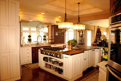 Example of a large eclectic dark wood floor kitchen design in St Louis with an undermount sink, raised-panel cabinets, white cabinets, wood countertops, stainless steel appliances and an island