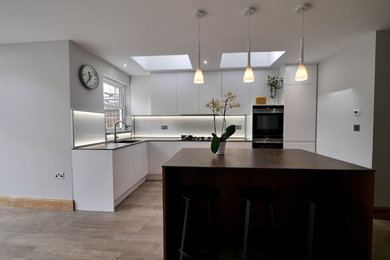 Medium sized contemporary l-shaped kitchen/diner in London with a submerged sink, flat-panel cabinets, purple cabinets, engineered stone countertops, white splashback, glass sheet splashback, black appliances, porcelain flooring, an island, brown floors and multicoloured worktops.