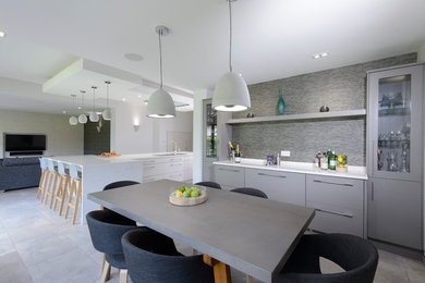 Große Moderne Küche mit Doppelwaschbecken, flächenbündigen Schrankfronten, grauen Schränken, Quarzit-Arbeitsplatte, schwarzen Elektrogeräten, Keramikboden, Kücheninsel und grauem Boden in Manchester