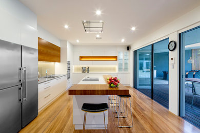 Design ideas for a large contemporary l-shaped separate kitchen in Adelaide with an integrated sink, flat-panel cabinets, white cabinets, quartz benchtops, metallic splashback, glass sheet splashback, black appliances, medium hardwood floors, with island and white benchtop.