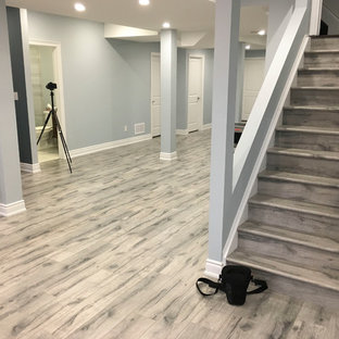 トロントの大きいモダンスタイルのおしゃれな地下室 (全地下、青い壁、ラミネートの床、吊り下げ式暖炉、タイルの暖炉まわり、グレーの床) の写真