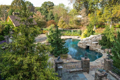 Large arts and crafts backyard custom-shaped natural pool in St Louis with a hot tub and natural stone pavers.