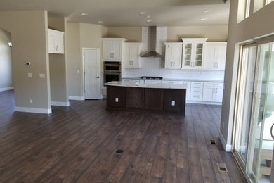 Huge trendy single-wall laminate floor and brown floor open concept kitchen photo in Denver with a farmhouse sink, shaker cabinets, white cabinets, quartzite countertops, white backsplash, subway tile backsplash, stainless steel appliances, an island and white countertops