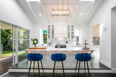 Inspiration for a large open plan kitchen in Sydney with shaker cabinets, white cabinets, an island, a belfast sink, engineered stone countertops, white splashback, engineered quartz splashback, black appliances, dark hardwood flooring, black floors and exposed beams.
