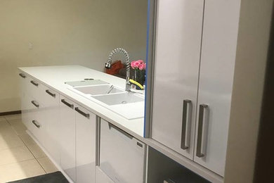 Small modern galley separate kitchen in Perth with an undermount sink, flat-panel cabinets, white cabinets, quartz benchtops, grey splashback, glass sheet splashback, stainless steel appliances, no island and white benchtop.
