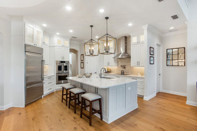 Large transitional l-shaped medium tone wood floor eat-in kitchen photo in Jacksonville with an island, an undermount sink, raised-panel cabinets, white cabinets, quartz countertops, beige backsplash, ceramic backsplash, stainless steel appliances and white countertops