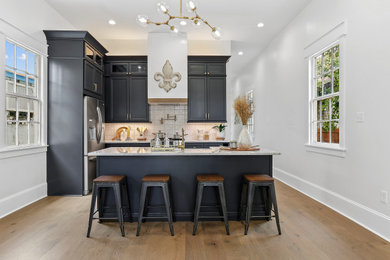 Example of a mid-sized arts and crafts l-shaped medium tone wood floor and brown floor eat-in kitchen design in New Orleans with a farmhouse sink, shaker cabinets, blue cabinets, marble countertops, beige backsplash, ceramic backsplash, stainless steel appliances, an island and white countertops