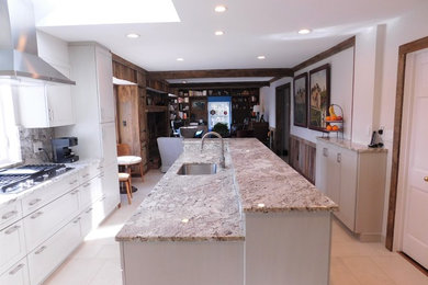 This is an example of a mid-sized transitional u-shaped open plan kitchen in DC Metro with an undermount sink, recessed-panel cabinets, white cabinets, marble benchtops, stainless steel appliances, ceramic floors, with island and white floor.