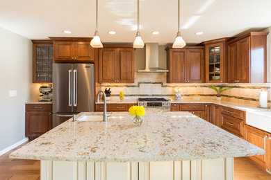 Inspiration for a large transitional l-shaped medium tone wood floor and brown floor eat-in kitchen remodel in Denver with a farmhouse sink, raised-panel cabinets, medium tone wood cabinets, granite countertops, beige backsplash, stone tile backsplash, stainless steel appliances and an island