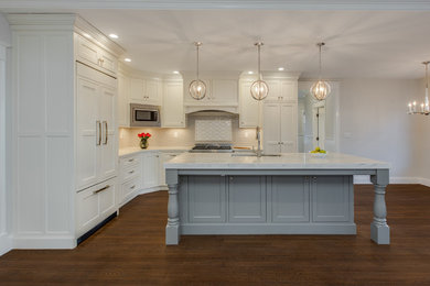 This is an example of a large transitional l-shaped open plan kitchen in Boston with an undermount sink, shaker cabinets, white cabinets, granite benchtops, white splashback, subway tile splashback, stainless steel appliances, medium hardwood floors, with island, brown floor and white benchtop.